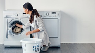 Mulher agachada coloca roupa na máquina de lavar roupa